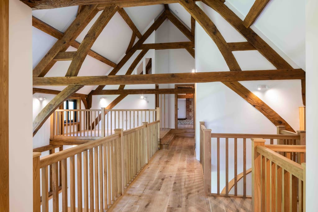 First-floor gallery landing beneath exposed oak roof trusses, with oak balustrades, wide oak floorboards and white plastered walls