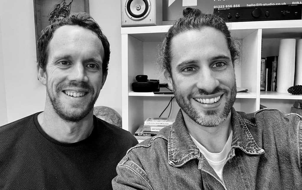 Black-and-white photograph of two members of the FT Studio team smiling in the studio, in front of white shelving with books and a speaker
