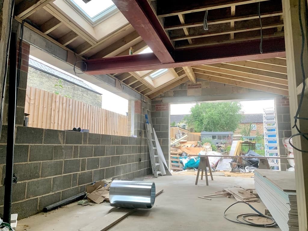 The extension mid-build: red-primed steel beams, timber roof joists and rooflights over blockwork walls, open to the garden