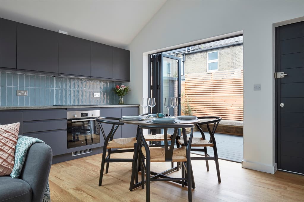 Dining area and dark grey kitchen with bi-fold doors open to a small decked courtyard with a slatted timber fence
