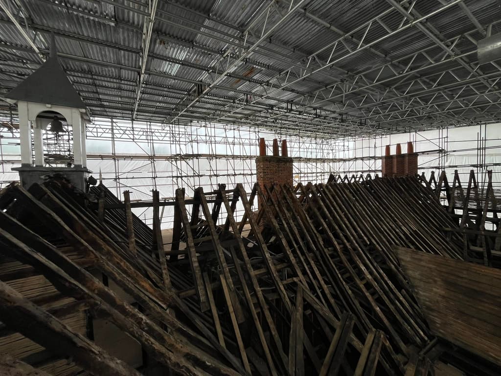 Campton Manor's roof stripped to blackened rafters beneath a temporary scaffold roof, with the bell turret and chimney stacks beyond