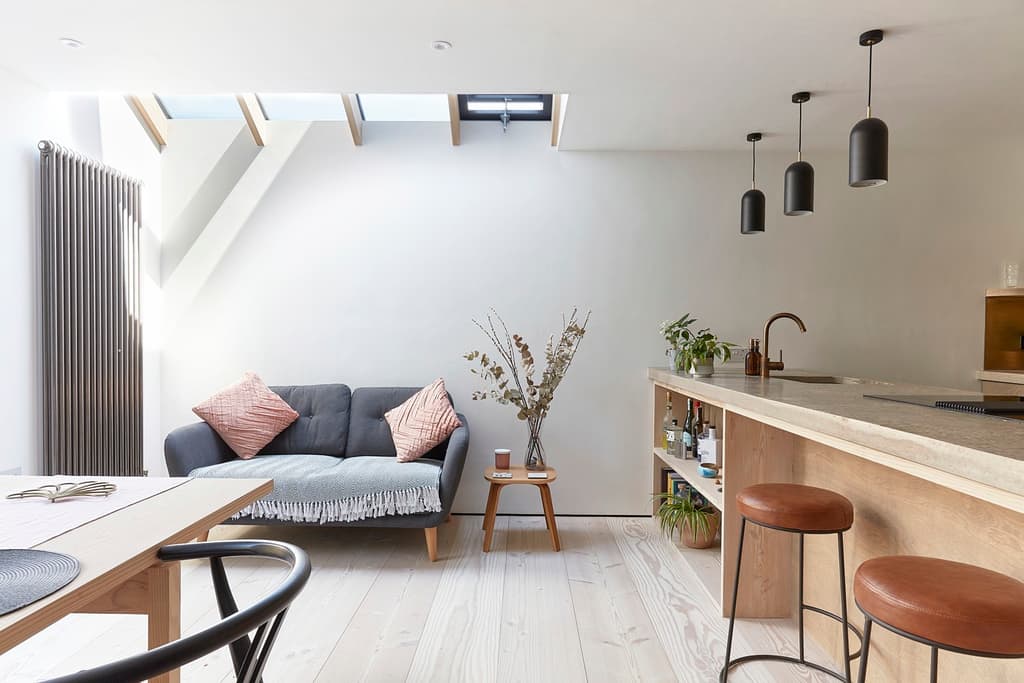 Open-plan living space with rooflights set between timber beams, a grey sofa and a concrete-topped kitchen island with leather stools